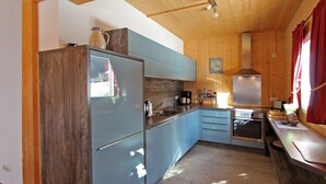 A kitchen with wooden cabinets, a stainless steel range hood, and a window with red curtains.