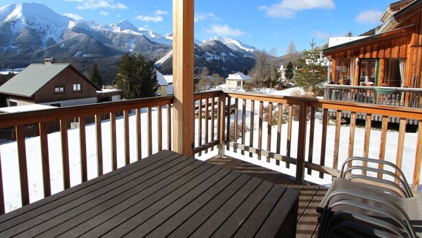 A wooden deck with a view of snow-covered mountains and buildings.