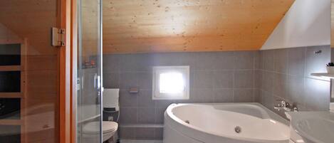 A bathroom with a large bathtub, a toilet, and a glass shower enclosure.