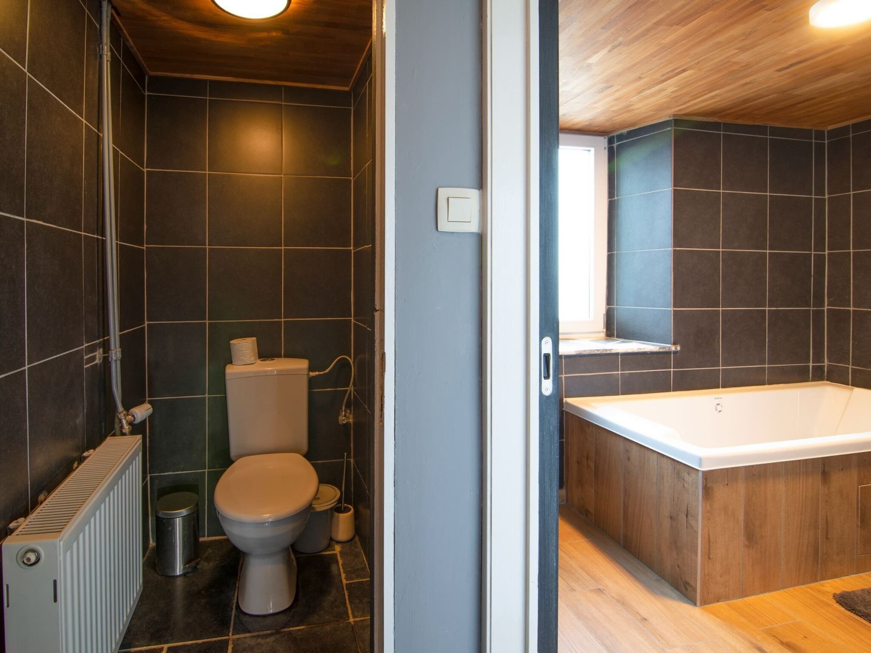 Et moderne badeværelse med mørke fliser, et hvidt toilet, et badekar og en radiator.
