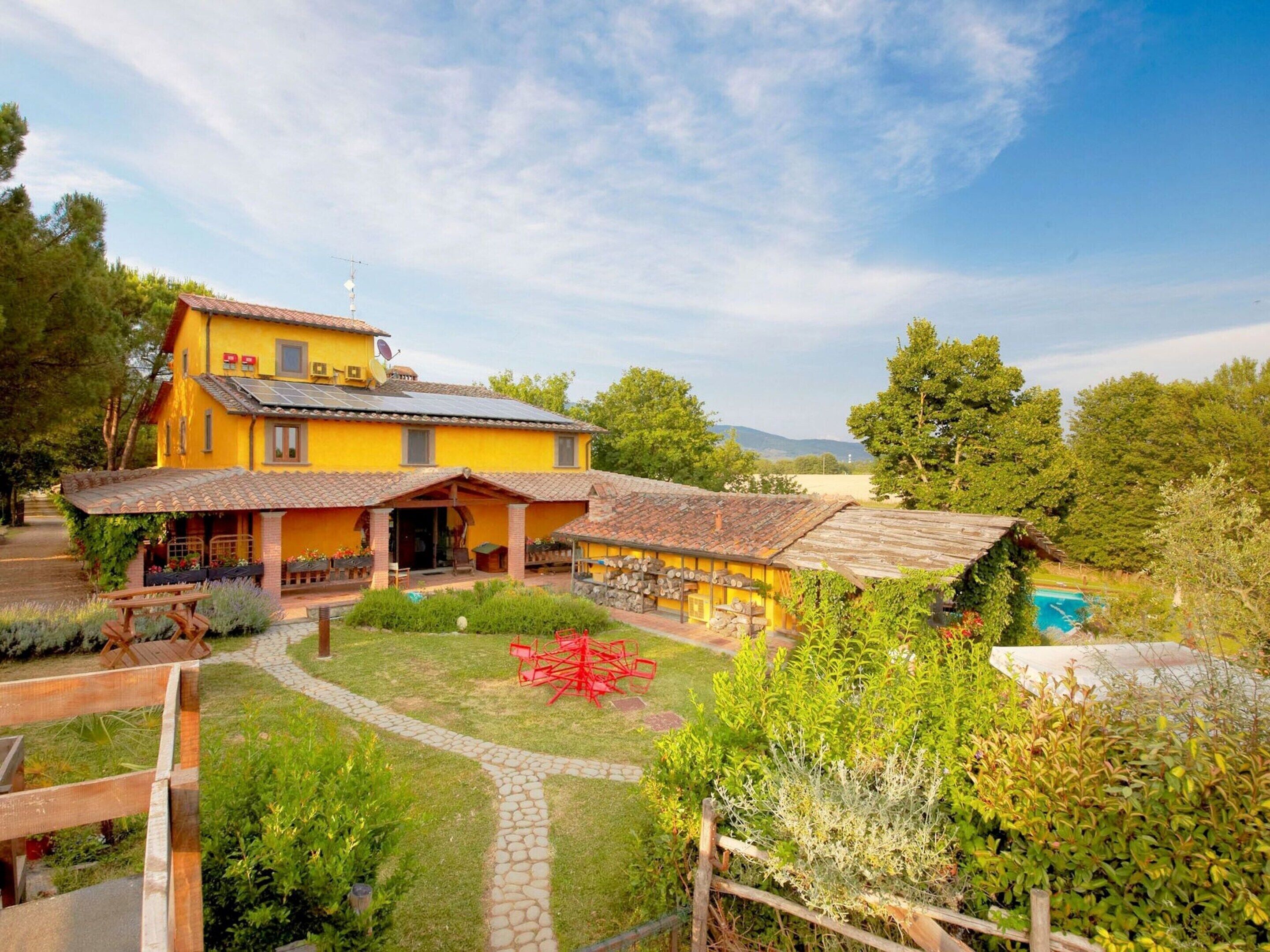 A yellow house with a tiled roof, a garden with a paved path, and a small pool.