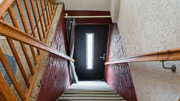 Een trap met houten leuningen, een zwarte deur aan de bovenkant en een structuurmuur.