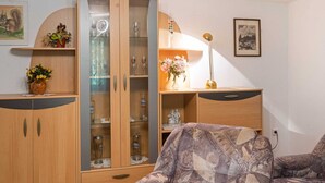 Een woonkamer met een houten kast, een gestreept fauteuil en een kleine tafel met een lamp.
