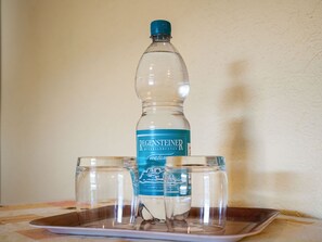 Une bouteille en plastique transparente, dotée d’un bouchon et d’une étiquette bleus, est posée sur un plateau avec trois verres vides.