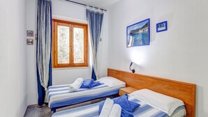 A room with two beds, a window with curtains, a nightstand, and wall-mounted pictures. - Restful Apartment in Cala Gonone with Balcony near Sea Beach (Dorgali)