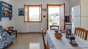 A compact living space with a dining area, a sofa, a bookshelf, and a view of the outside. - Restful Apartment in Cala Gonone with Balcony near Sea Beach (Dorgali)