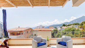 A balcony with wicker furniture, a potted plant, and a view of houses and mountains. - Restful Apartment in Cala Gonone with Balcony near Sea Beach (Dorgali)