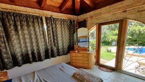 Ein Schlafzimmer mit Bett, Kommode, Spiegel und Blick auf einen Swimmingpool durch eine Glastür.
