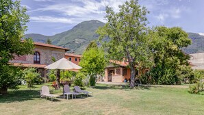 A rustic villa with a stone facade, a patio with a table and chairs, and a view of mountains in the background. - Villa With Garden Near Versilia Beach (Camaiore)