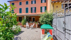 A courtyard with a play area, a brick patio, and a building with multiple windows and shutters. - Villa With Garden Near Versilia Beach (Camaiore)