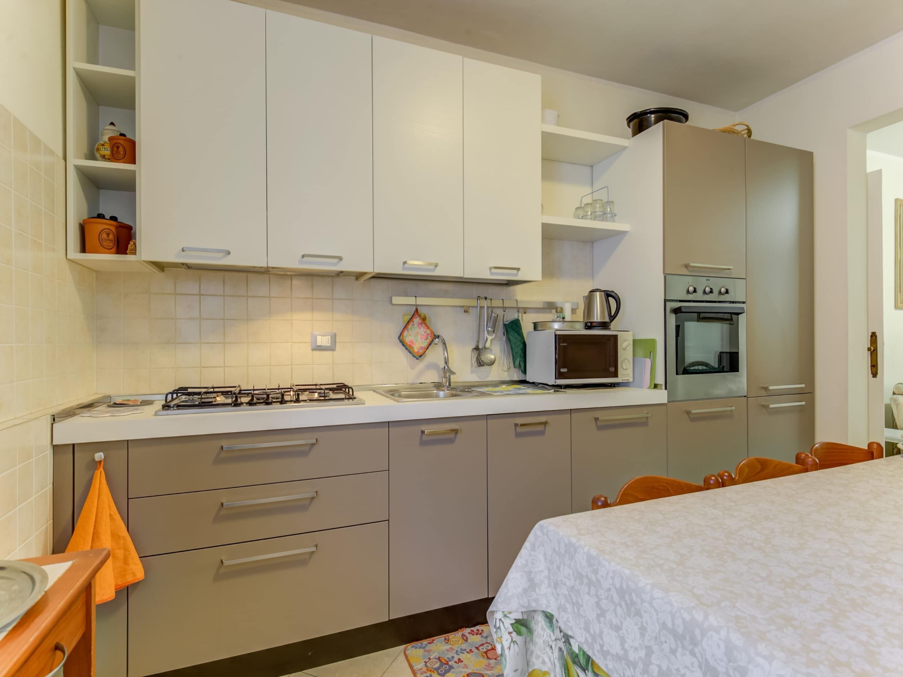 A kitchen with white cabinets, a gas stove, a microwave, and an oven. There is a dining table with chairs and a rug.