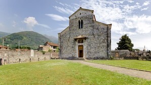 A stone church with a central nave and a bell tower, surrounded by a stone wall and a grassy area. - Villa With Garden Near Versilia Beach (Camaiore)