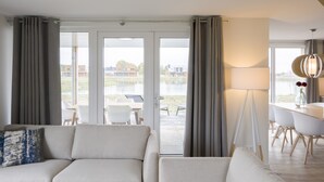 Una sala de estar moderna con un sofá, una mesa de comedor con sillas y vistas a un lago a través de amplios ventanales.