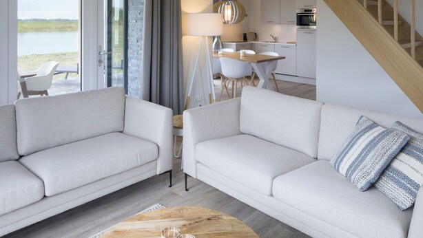 Una sala de estar moderna con dos sofás, una mesa de centro y vistas a una cocina y comedor.