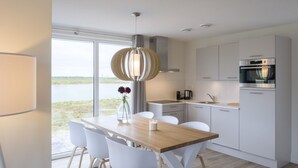 Una cocina moderna con armarios blancos, una mesa de comedor de madera y vistas a un cuerpo de agua.