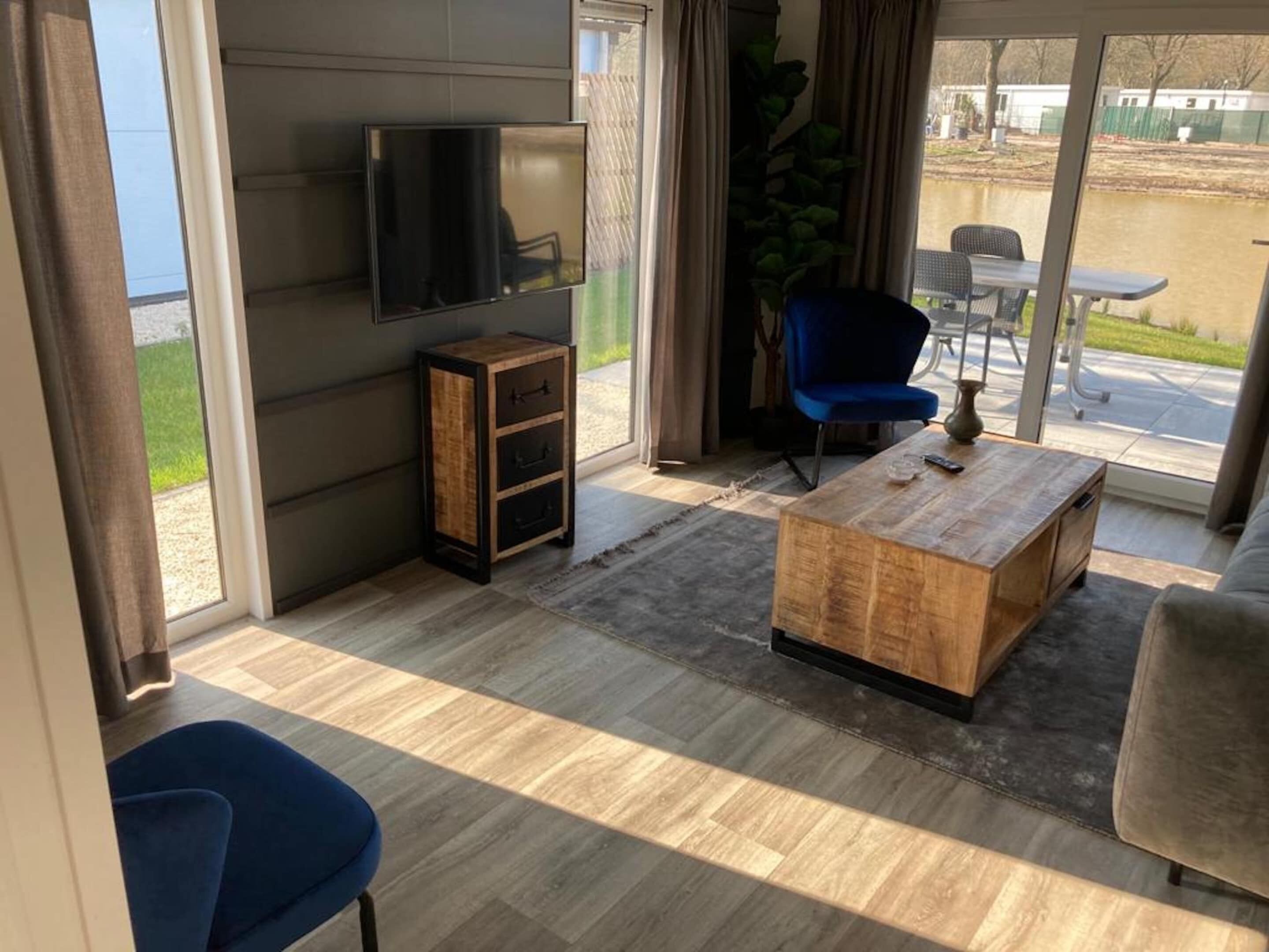 A modern living room with a flat-screen TV, a wooden coffee table, a blue chair, and a sofa.