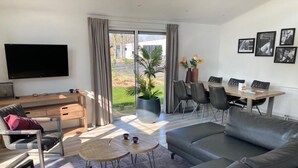 A modern living room with a grey sofa, a coffee table, a TV, and a dining area with chairs and a table. - Modern Chalet With Combi Microwave Near Efteling (Kaatsheuvel)