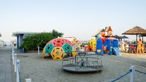 Ein Strandbereich mit Spielplatz, Sitzgelegenheiten und einem kleinen Gebäude.
