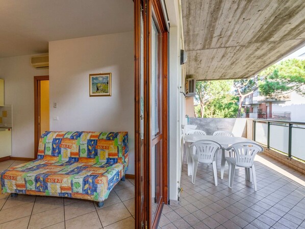 A balcony with a sofa and chairs, a painting on the wall, and a view of greenery outside.