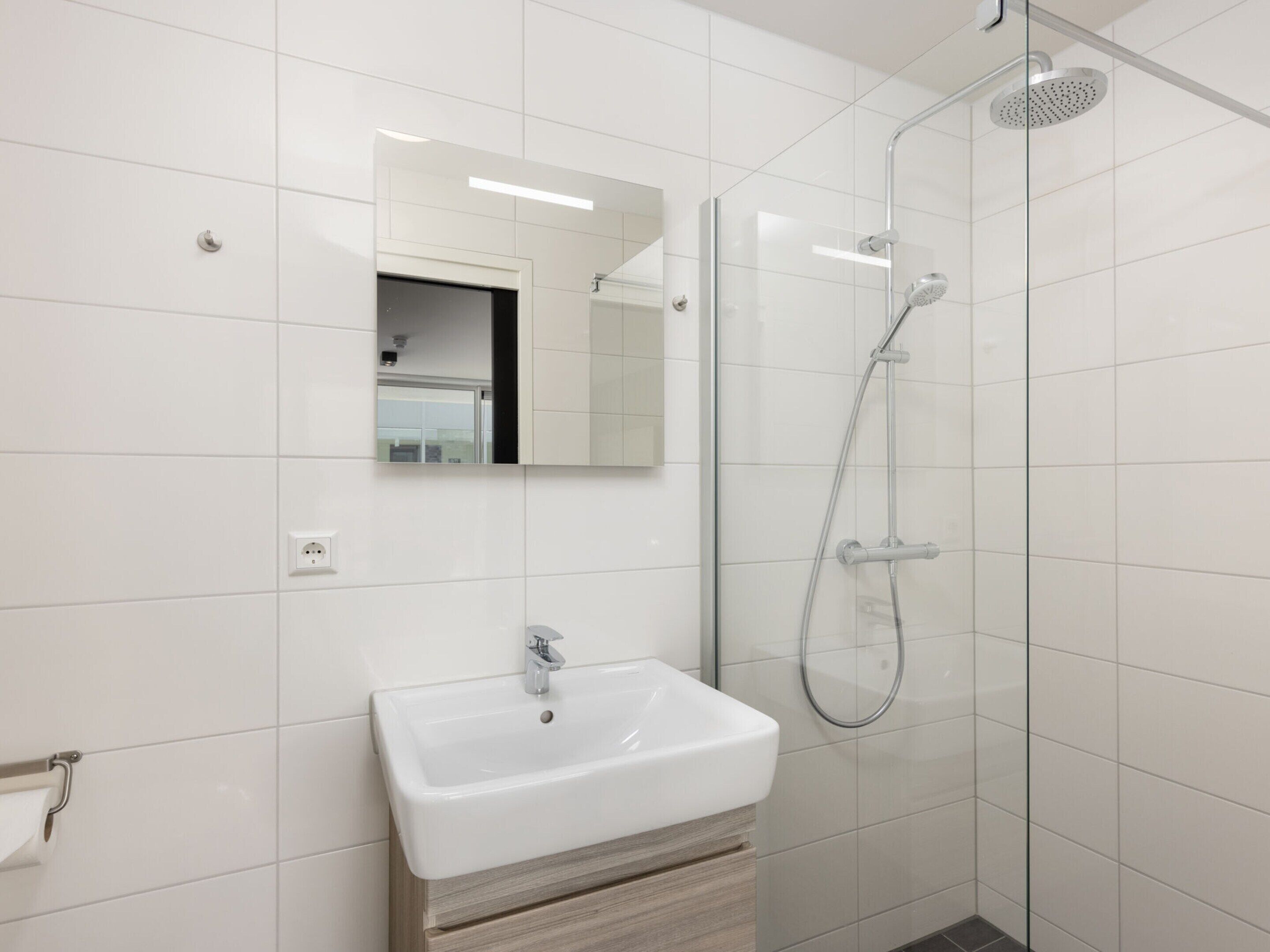 A modern bathroom with a white sink, mirror, and glass shower enclosure.