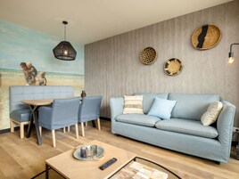 A living room with a blue sofa, a dining table with chairs, a painting of a beach scene, and decorative wall art.