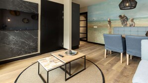 Een moderne woonkamer met een houten salontafel, een bank en een muurschildering van kinderen op het strand.