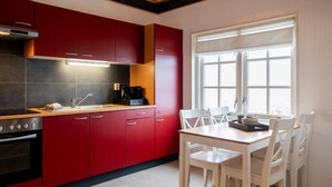 A modern kitchen with red cabinets, a wooden countertop, and a dining area with a white table and chairs. - Chalet in Friesland Near Alde Feanen (De Veenhoop)
