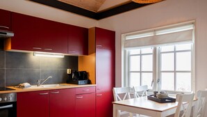 A modern kitchen with red cabinets, a white dining table, and a window with blinds. - Chalet in Friesland Near Alde Feanen (De Veenhoop)