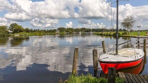 A calm lake with a red boat docked at a wooden pier. - Chalet in Friesland Near Alde Feanen (De Veenhoop)