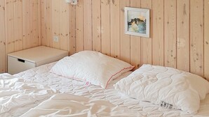 Ett sovrum med en väggpanel av trä, en vit säng med ett täcke, ett nattduksbord och en inramad tavla.