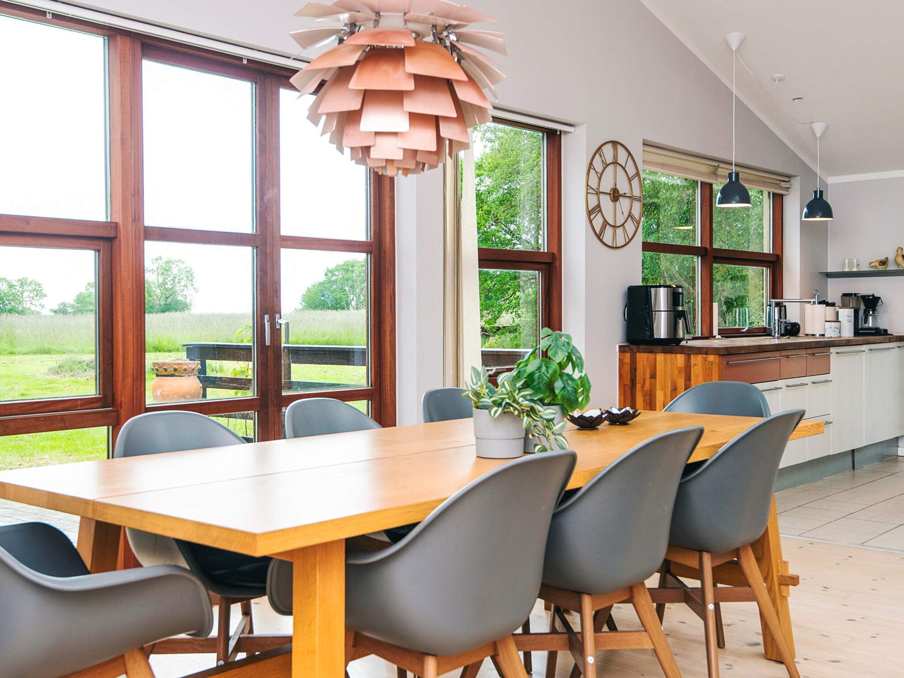 Une cuisine moderne avec de grandes fenêtres, une table à manger en bois et des chaises grises.