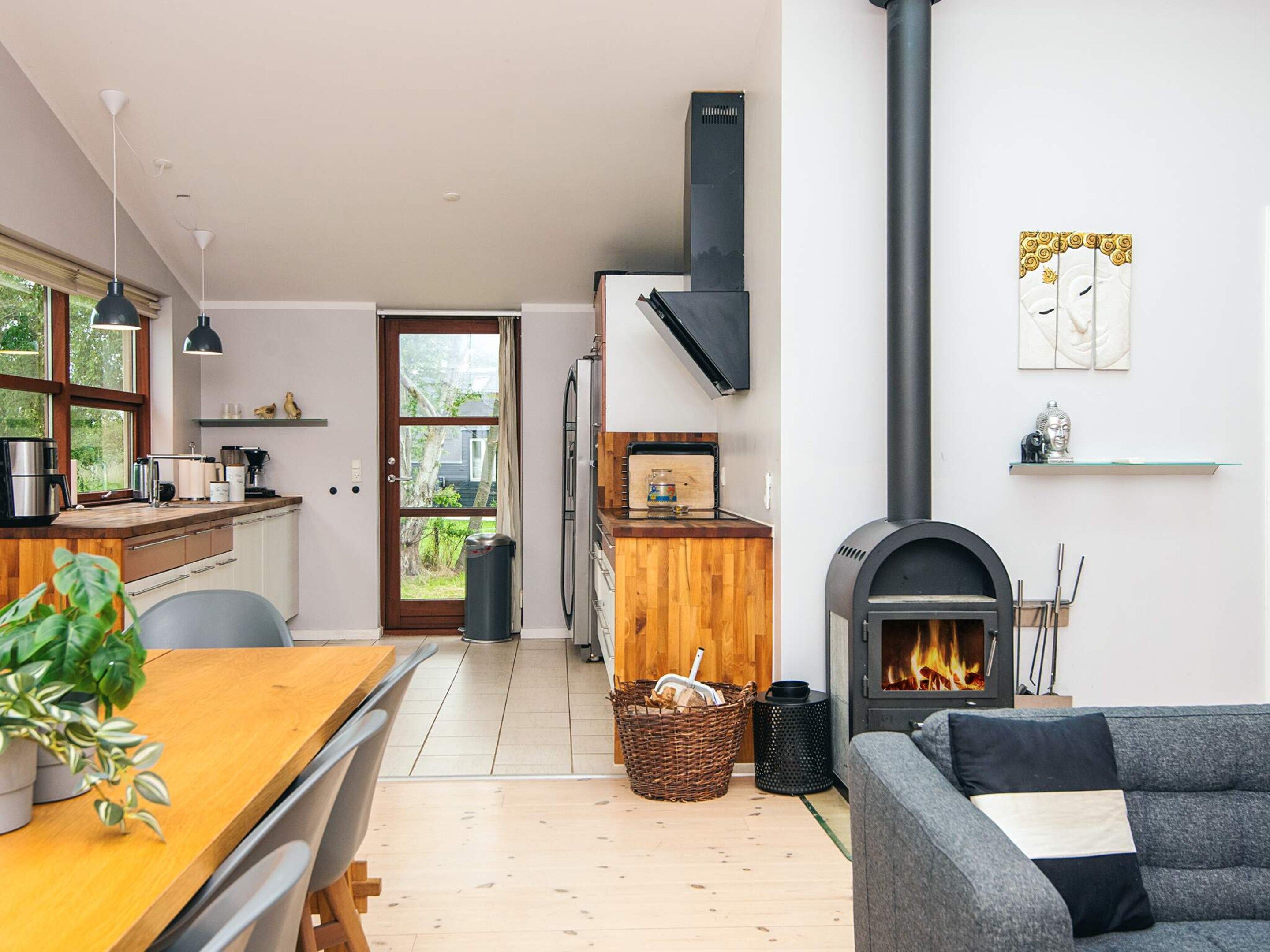 A modern kitchen with a large window, a dining area with a wooden table, and a living room with a fireplace.