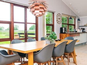 A modern kitchen with large windows, a wooden dining table, and grey chairs. - Holiday Home in Knebel (Knebel)