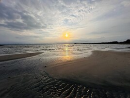 A beach with a sunset, calm waters, and a clear sky.