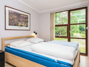 A bedroom with a bed, a nightstand, a framed picture, and a window with a view of greenery. - Holiday Home in Knebel (Knebel)