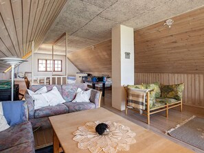 A cozy loft-style living space with a sofa, a wooden coffee table, and a patterned armchair. - 6 Person Holiday Home in Thyholm (Thyholm)