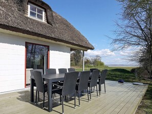 A thatched-roof house with a white exterior, a deck with outdoor furniture, and a view of the landscape. - 6 Person Holiday Home in Thyholm (Thyholm)