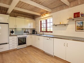 Ett kök med vita skåp, ett träpanelat tak, ett fönster med röda gardiner och en hylla med dekorativa föremål.