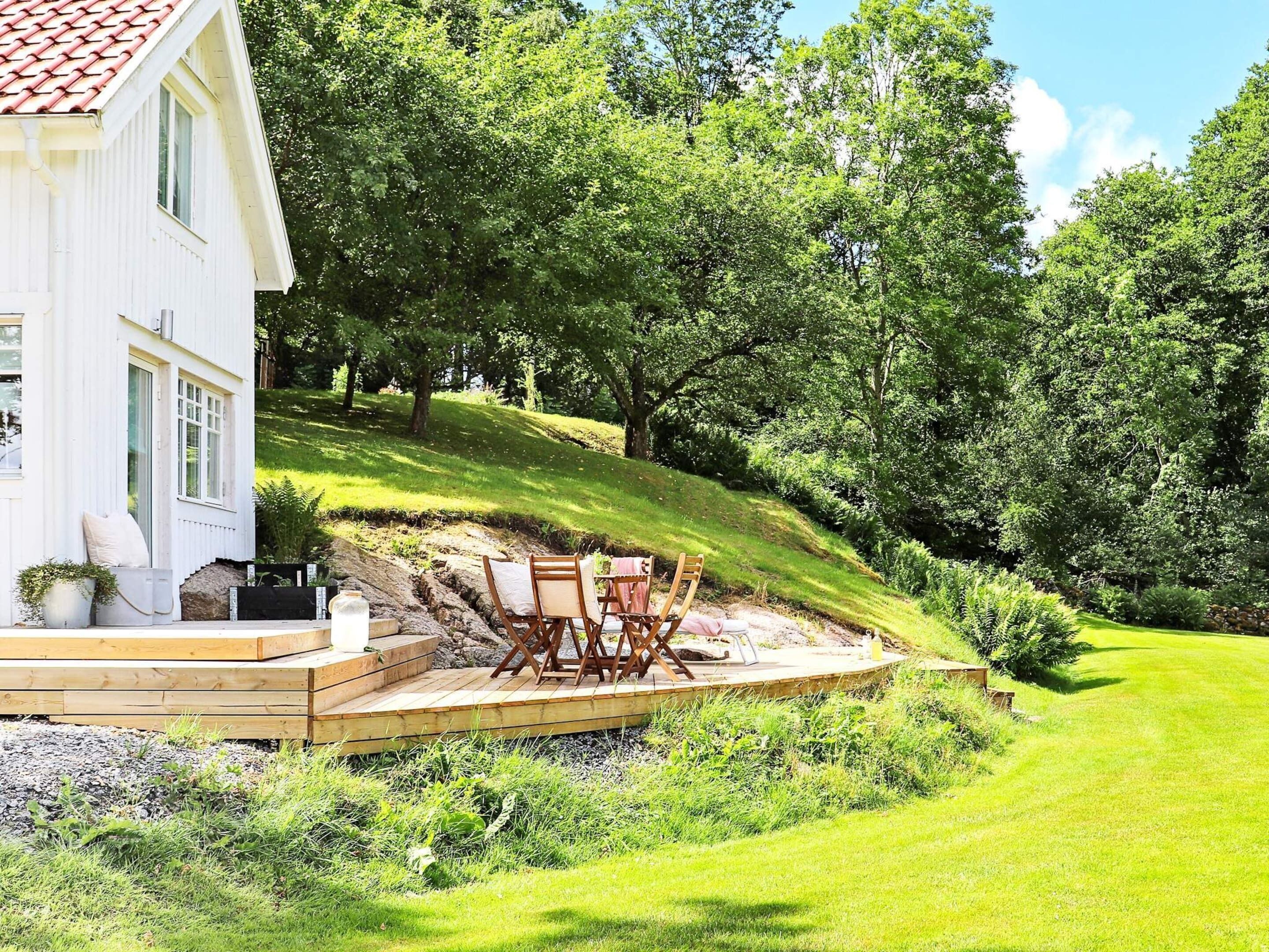Et hvidt hus med terrasse, udendørs siddepladser og et frodigt grønt landskab.