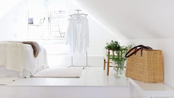 A minimalist bedroom with a bed, a hanging chair, a woven basket, and a small plant.