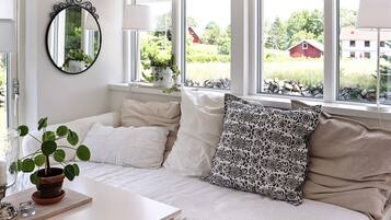 A room with a bed, a bedside table, a mirror, and a window with a view of greenery and buildings.