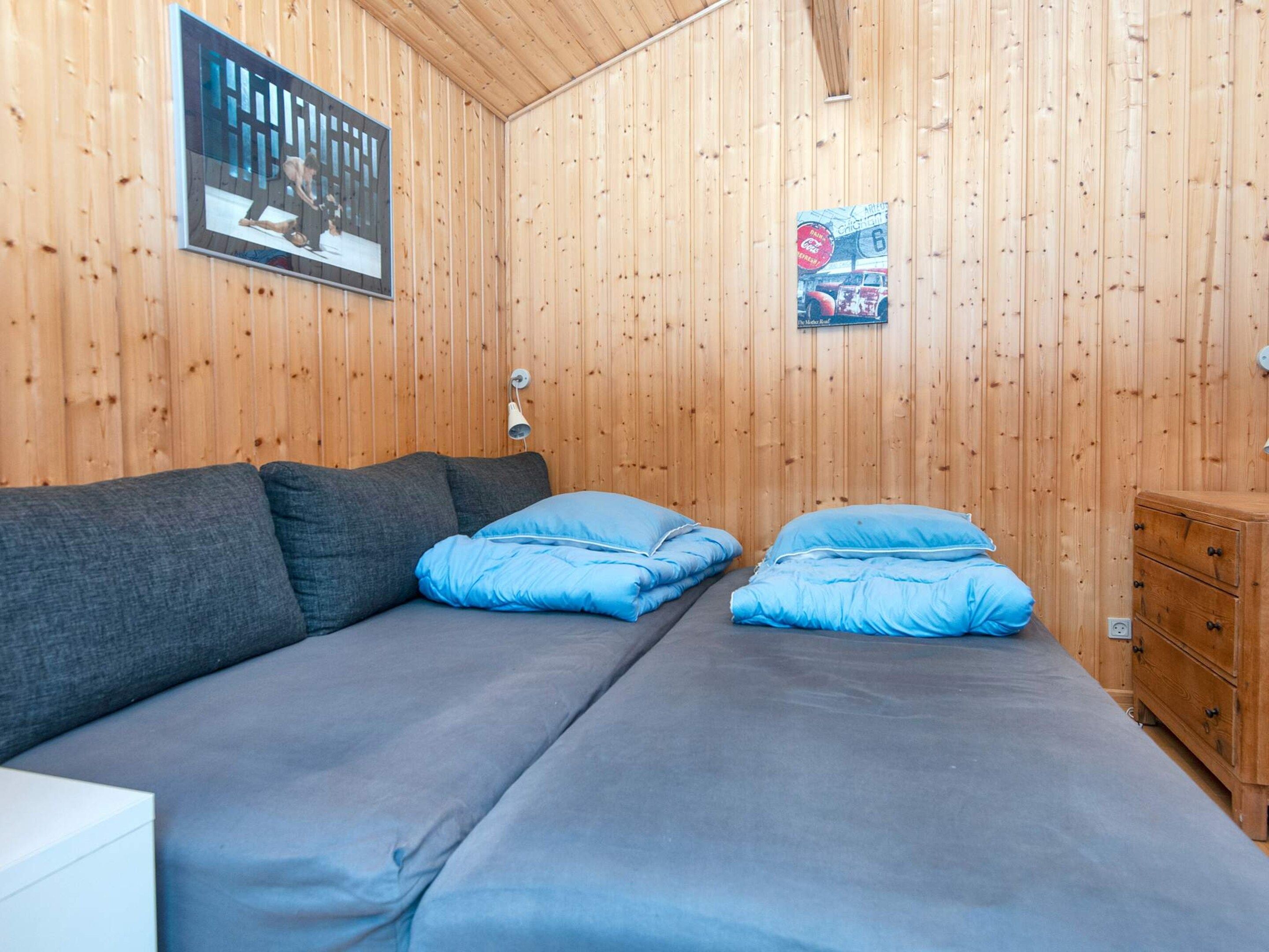 A room with a wooden wall, a sofa with blue and gray cushions, a small wooden dresser, and a poster on the wall.
