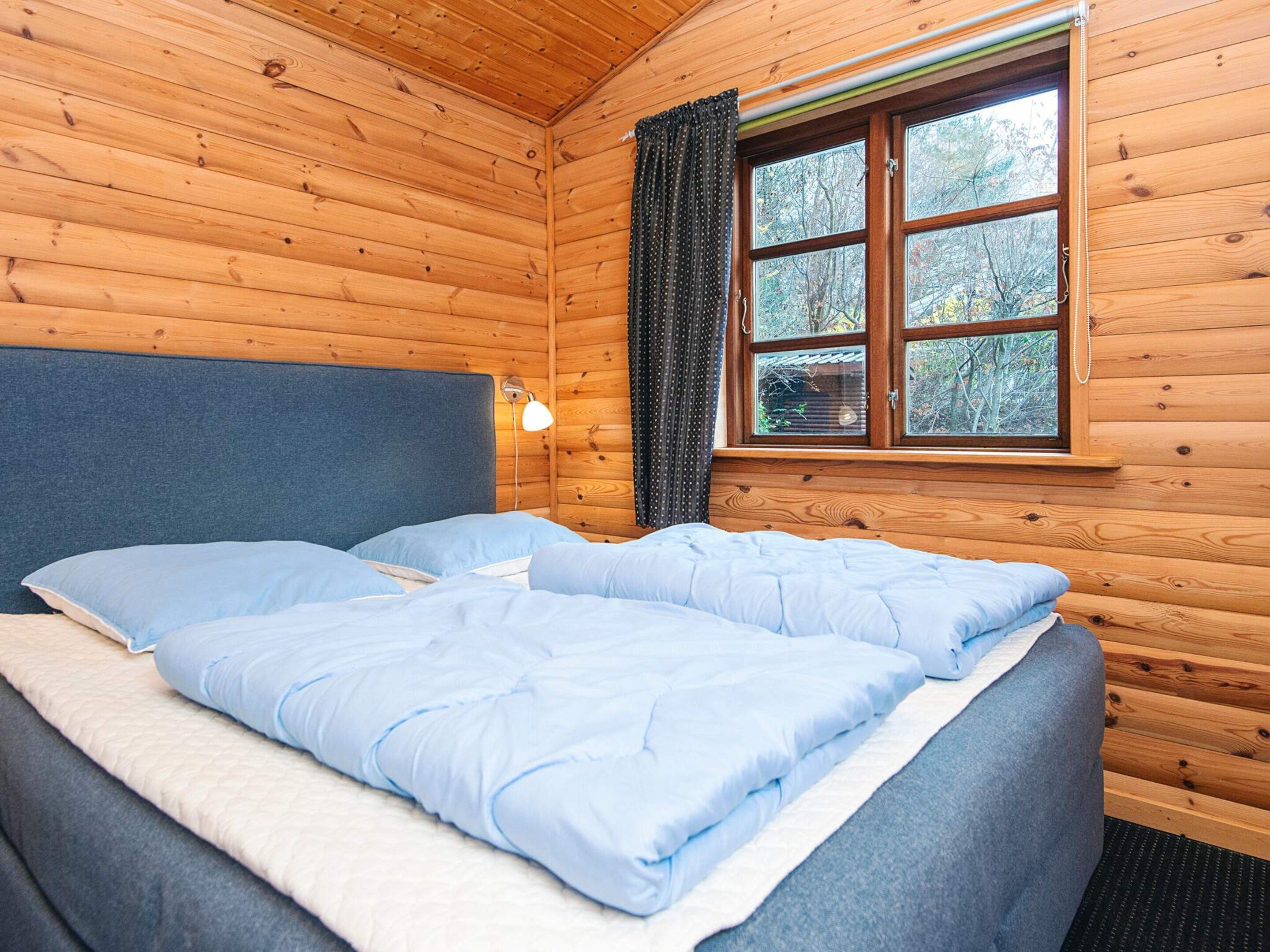 Ein Zimmer in einer Holzhütte mit einem Bett, einem Fenster und einer Lampe.