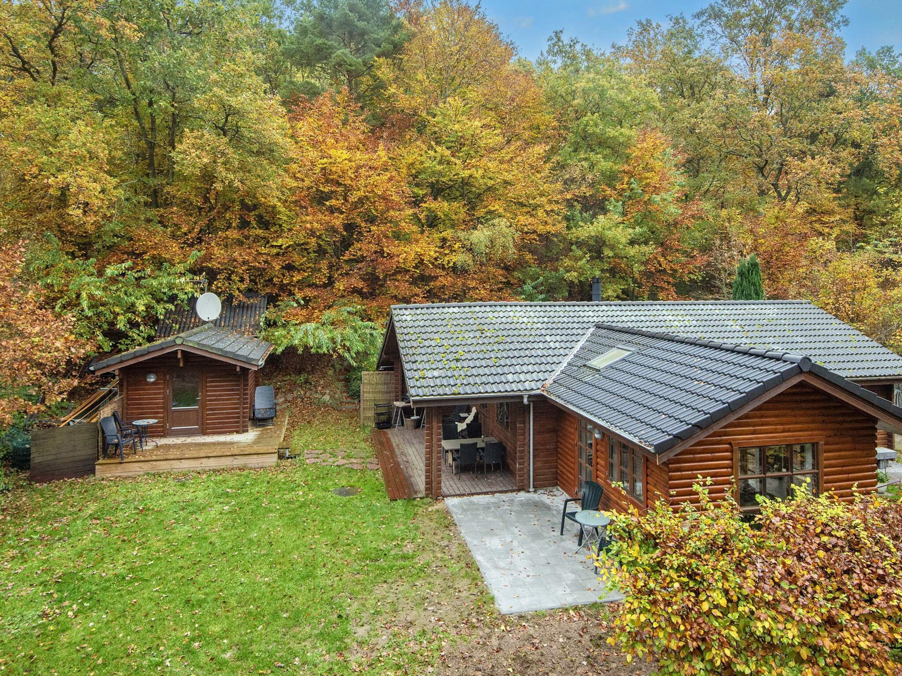 Een chalet met een terras en een houten vlonder, omgeven door herfstbladeren.