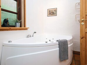 A bathroom with a white bathtub, a wooden door, a small framed picture on the wall, and a potted plant. - 4 Star Holiday Home in Ebeltoft (Ebeltoft)