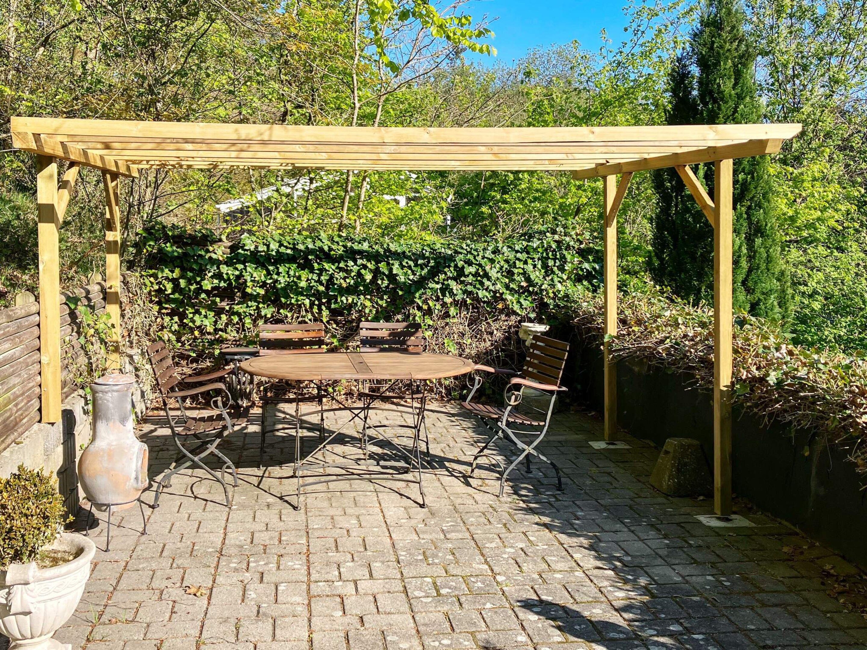 A patio with a wooden pergola, a round table, and four chairs.