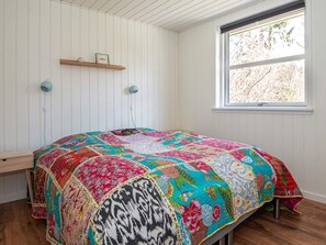 A bedroom with a large bed, a window, and a wooden shelf.