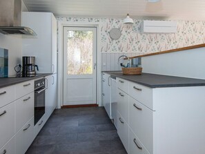 A compact kitchen with white cabinetry, a coffee maker, and a window with a view of trees. - Holiday Home in Silkeborg (Silkeborg)