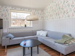 Et værelse med en grå sofa, et rundt sort bord og en hængende lampe.