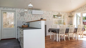 Una cocina con una isla central, un comedor con mesa y sillas, y un ventanal con vistas a árboles.